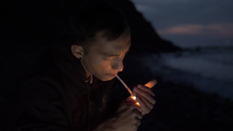 Junger-Nepalesischer-Mann,-Der-Nachts-Allein-Am-Strand-Sitzt-Und-Sich-Eine-Zigarette-Anzündet