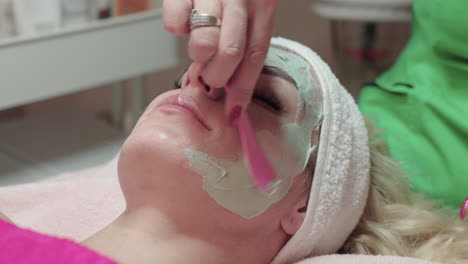 Kosmetikerin,-Die-Eine-Gesichtsmaske-Für-Die-Peeling-Behandlung-Auf-Dem-Gesicht-Der-Frau-Im-Spa-Salon-Aufträgt,-Nahaufnahme