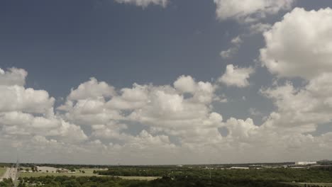 A-small-jet-flies-in-the-blue-skies-and-puffy-white-clouds-above-highways-surrounded-by-green-trees