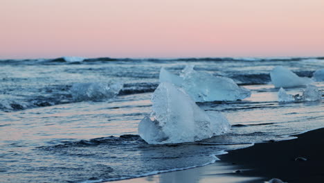 Gentle-waves-break-around-small-ice-chunks-on-black-sand,-Diamond-Beach,-Iceland