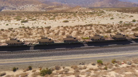 Vista-Aérea-De-Cientos-De-Tanques-Del-Ejército-Estadounidense-Que-Se-Transportan-A-Través-Del-Desierto-En-Tren