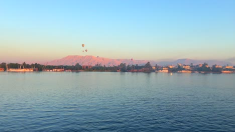4K-static-scenic-clip-of-several-hot-air-balloons-flying-over-the-Valley-of-the-Kings-and-the-Egyptian-Nile-River-at-sunrise