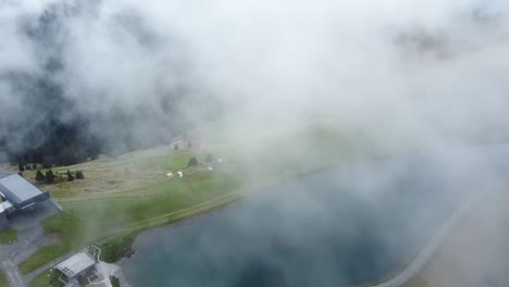 Drone-pans-camera-with-the-clouds-hovering-over-a-beautiful-small-reservoir-on-the-mountain-Asitz-Kogel-in-Austria,-Leogang-Saalbach