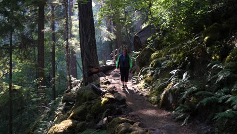 Senior-woman-walks-down-a-forest-path-with-light-beams-shining-through-the-canopy