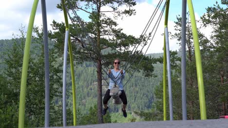 Childish-adult-woman-having-fun-riding-chain-and-rope-swing-inside-Bjorneparken-theme-park-in-Norway