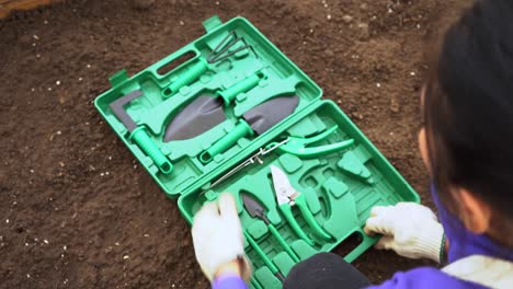 Female-Gardener-Opens-Green-Tool-Box-With-Set-Of-Gardening-Tools-On-The-Ground