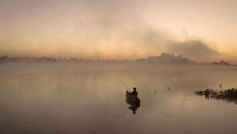 Aerial-of-a-man-that-is-fishing-by-himself-in-a-lake-before-sunrise,-Imire,-Zimbabwe