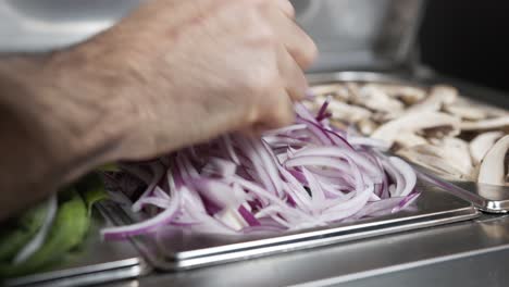 A-skilled-chef's-hand-takes-a-handful-of-onions-from-the-metal-tray