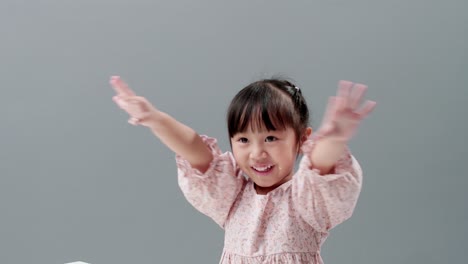 Little-Asian-girl-wearing-dress-smiling,-waving-hands-and-looking-at-camera-in-studio