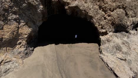Downward-aerial-shot-of-Bethells-Beach-with-a-man-walking-into-the-cave