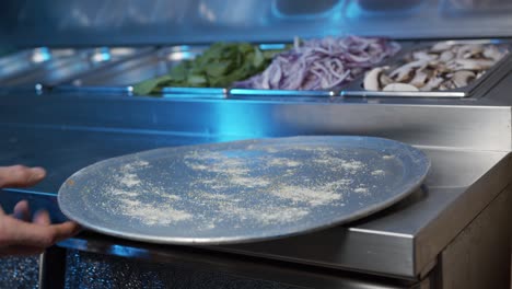 A-close-up-of-a-skilled-chef's-hands-put-pizza-tray-on-a-steel-counter-while-camera-pan-with-his-movement