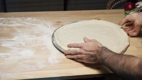 A-top-shot-of-a-skilled-chef's-hands-put-pizza-dough-on-a-steel-tray-on-wooden-counter,-shallowing-it-and-set-it-up-for-the-oven
