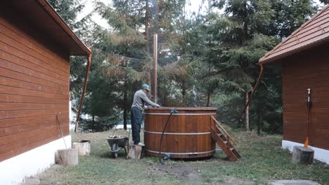 Man-Alight-The-Fire-For-Traditional-Hot-Tub-Between-The-Wooden-Houses