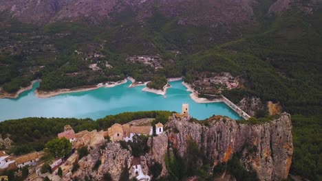 Cinematic-panoramic-drone-4K-view-of-a-medieval-castle´s-battlement-on-top-of-a-village-where-a-large-reservoir-of-turquoise-waters-is-observed