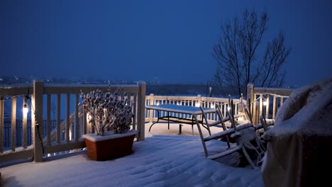 A-backyard-deck-on-a-snowy-night-with-the-porch-light-son-and-the-dining-table-covered-in-snow---static-wide-angle-view