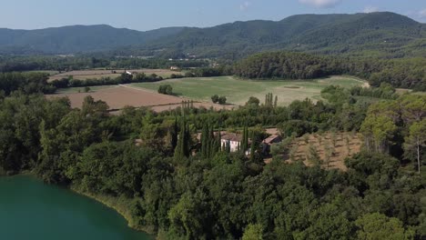 Aerial-view-over-a-beautiful-landscape-with-a-natural-lake-surrounded-by-woods,-and-farmlands-in-the-Spanish-countryside