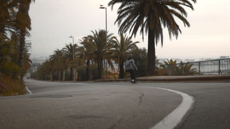 Carefree-young-man-skates-downhill-in-road,-scenic-view,-low-angle,-gimbal