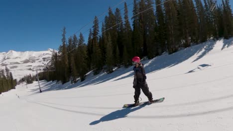 Female-snowboarder-riding-goofy-down-Colorado-ski-resort-on-a-bluebird-day