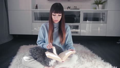 Young-attractive-woman-reading-a-book-sit-cross-legged-on-hairy-rug-in-her-modern-living-room,-caucasian-female-relaxing-alone-at-home