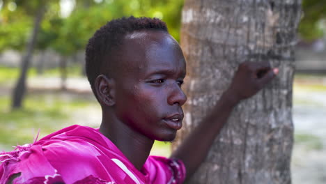Native-african-maasai-man-leaning-on-palm-tree-with-left-arm,-close-up