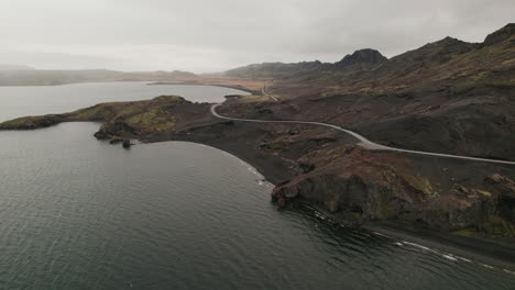 Aerial-rise-above-winding-highway-running-along-shore-of-lake-in-Iceland