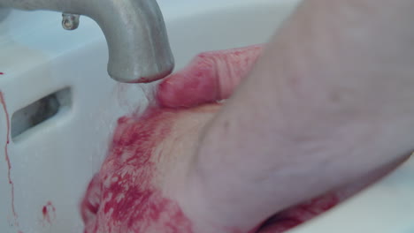 Close-up-of-a-man-washing-blood-off-his-hands-in-a-bathroom-sink