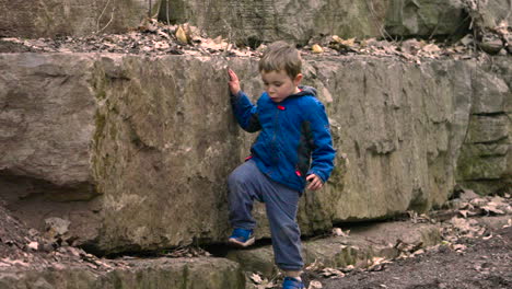 Young-boy-exploring-and-climbing-on-a-rock-wall-in-the-forest