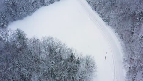 Aerial-top-down-flying-above-a-snow-covered-landscape-with-a-road-winding-along-forests-and-fields-SLOW-MOTION