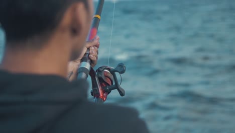 Young-man-spin-fishing-at-seashore-over-shoulder-shot