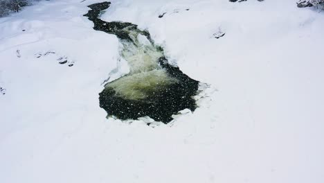 Flying-down-and-tilting-up-on-a-small-water-fall-on-a-frozen-river-during-a-snow-storm-Slow-motion-aerial