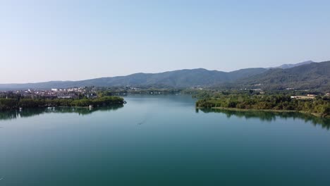 Panoramic-view-over-a-scenic-landscape-with-a-natural-lake-surrounded-by-trees-and-a-town,-nearby-the-mountains,-Spain