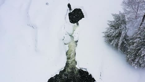 Während-Eines-Schneesturms-In-Zeitlupe-In-Richtung-Eines-Kleinen-Wasserfalls-Auf-Einem-Zugefrorenen-Fluss-Fliegen