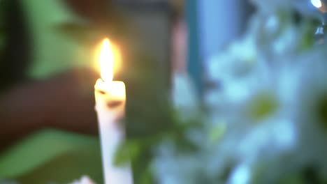 A-candle-burns-as-the-camera-rolls-focus-to-flowers-in-the-foreground