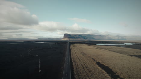 Flyover-above-long-straight-highway-through-black-sand-desert-in-Iceland
