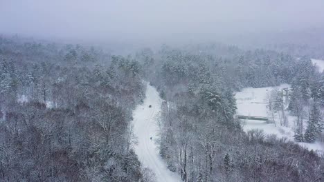 Flying-high-above-a-road-and-river-winding-through-a-forest-during-a-snow-storm-SLOW-MOTION-AERIAL