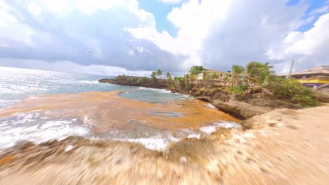 Fpv-flight-over-green-water-and-beautiful-coastline,-palm-trees-and-playground-during-sunny-day---Boca-de-Yuma,Dominican-Republic