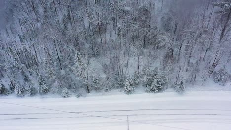 Aerial-slide-along-a-snow-covered-road-and-forest-during-a-snow-storm-TOP-DOWN-SLOW-MOTION