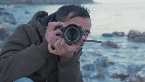 Young-Nepali-man-looking-through-camera-viewfinder-at-rocky-coastline