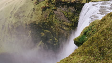 Powerful-water-pours-over-mossy-cliff-at-top-of-Skogafoss-Waterfall,-Iceland