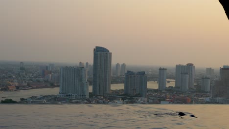 person-swimming-in-an-infinity-pool-on-a-high-rise-in-Bangkok-with-a-river-view-of-the-skyline-in-Thailand
