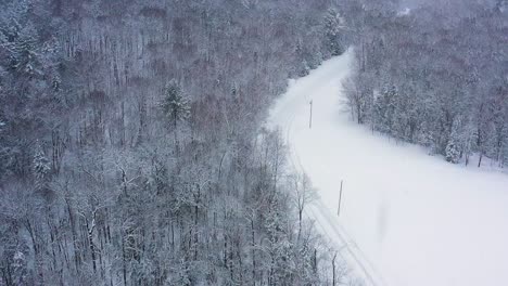 Tilting-up-away-from-a-road-winding-through-a-forest-during-a-snow-storm-to-reveal-distance-obscured-by-the-storm-SLOW-MOTION-AERIAL