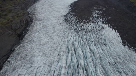Inclinación-Aérea-Hacia-Arriba-Del-Glaciar-En-Islandia-Que-Fluye-Montaña-Abajo-Entre-Dos-Crestas