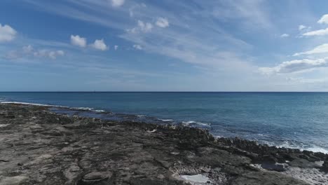 Drone-flying-over-man-on-volcanic-rocks-at-Ko-olina-beach-shore,-Hawaii
