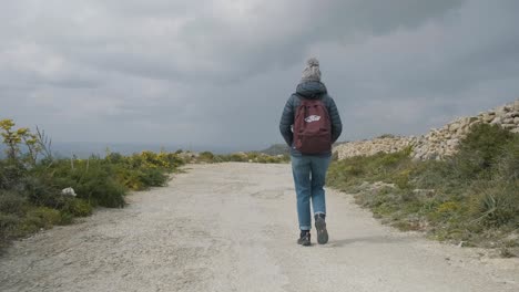 Young-woman-walking-on-a-rural-road-during-a-day-trip-in-the-mediterranean-nature-on-a-cloudy-winter-day
