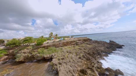 Drone-flight-over-tropical-Coastline-of-Caribbean-Sea-during-cloudy-and-sunny-day---Growing-plants-,rocky-cliffs-and-splashing-water