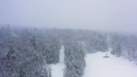 Flying-backwards-through-a-blizzard-above-a-frozen-river-and-forest-slow-motion-aerial