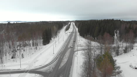 Aerial,-drone-shot,-over-traffic-on-road-6,-surrounded-by-snowless-trees,-cars-turning-right-and-left-at-crossings-and-intersections,-on-a-cloudy,-winter-day,-in-Kontionlahti,,-North-Karelia,-Finland