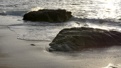High-Angle-Shot-Detail-Von-Zwei-Felsen-Am-Strand,-Die-Bewegung-Der-Meereswellen-Während-Des-Sonnenuntergangs