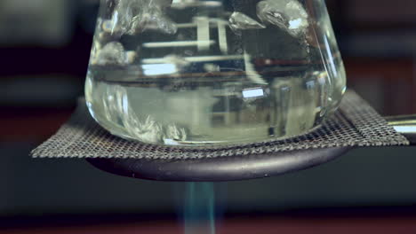 Close-up-of-bottom-of-water-boiling-in-an-erlenmeyer-flask-on-a-ring-stand-heated-by-bunsen-burner