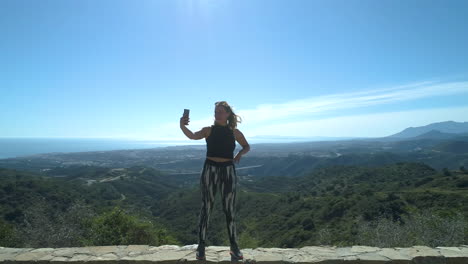 Aerial-arc-shot-of-female-in-gym-outfit-video-blogging-about-the-fantastic-nature-in-Marbella,-Spain
